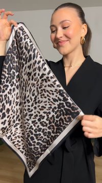 Sidenscarf med leopardmönster på en ljusbeige bakgrund och kontrasterande svart kant, som visar en mjuk textur och livfullt mönster.