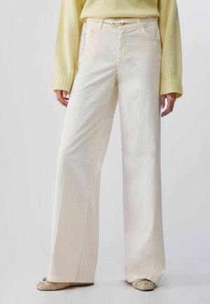 Pantaloni crema a gamba larga con tasche frontali, cintura con fibbia argento, abbinati a ballerine crema con borchie e pullover giallo chiaro con polsini a coste.