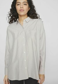 Camisa de botones a rayas en gris claro con líneas sutiles. Presenta un collar, mangas largas y un bolsillo en el pecho. Fabricada con un tejido ligero.