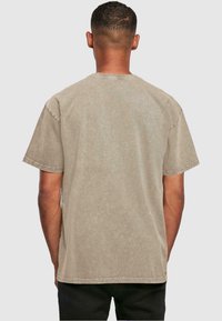 Beige bomulds t-shirt med en afslappet pasform, korte ærmer og rund hals. Synlige sømme langs sømmene. Bagfra.