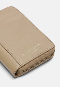 Beżowy skórzany portfel z zamkiem błyskawicznym, trzema kieszonkami na karty, teksturowaną powierzchnią oraz złotym logo "LIEBESKIND BERLIN" z przodu.