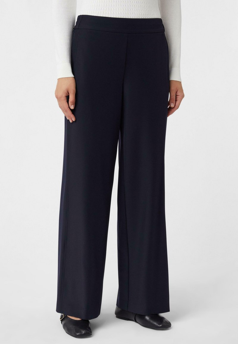 Pantalons larges marine à la texture douce, dotés d'une taille sans couture et de poches latérales, associés à des chaussures plates noires.