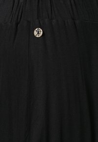 Tissu noir avec un détail froncé et un petit bouton décoratif rond en or présentant un motif découpé.