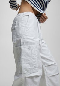 Witte cargo broek met een elastische tailleband, meerdere zakken en een relaxte pasvorm, gemaakt van een gestructureerde stof met zichtbare stiksels.