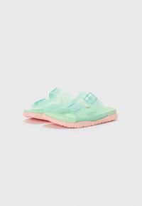 Gjennomsiktige mintgrønne sandaler med bred reim og justerbar spenne, med en teksturert såle og myk rosa yttersåle.