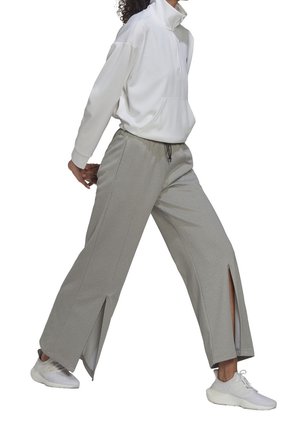 Jasnoszare spodnie dresowe z bocznymi rozcięciami, zestawione z białą bluzą z kapturem na zamek i białymi tenisówkami. Codzienny strój sportowy o luźnym kroju.