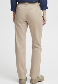Beige rechte broek met een gladde textuur, achterzakken en een riemlus, gecombineerd met lichtgekleurde, schoenen met dikke zolen.