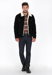 Schwarze Wildlederjacke mit einem cremefarbenen Kunstfellkragen, kombiniert mit einem karierten Hemd und dunklen Jeans, getragen mit schwarzen Kampfstiefeln.
