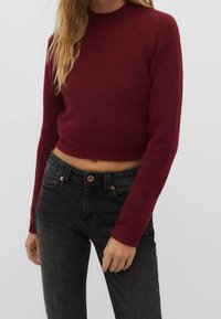 Burgundy cropped sweater with long sleeves, ribbed neckline and hem, made from textured knit material, paired with black jeans featuring a button closure.