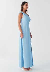 Helehall sinine, varrukateta maksikleit drapeeritud ülakehaosaga, ühe õlaga sõlme detaili ja kõrge lõhikuga. Silmapaistev, voolav kangas.