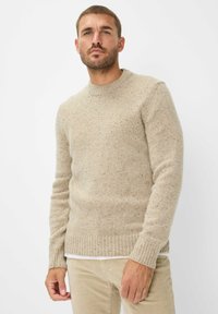 Beige Strickpullover mit rundem Ausschnitt, gerippten Bündchen und Saum, einem gefleckten Design und einer taillierten Passform. Betont durch ein schlichtes weißes Hemd darunter.