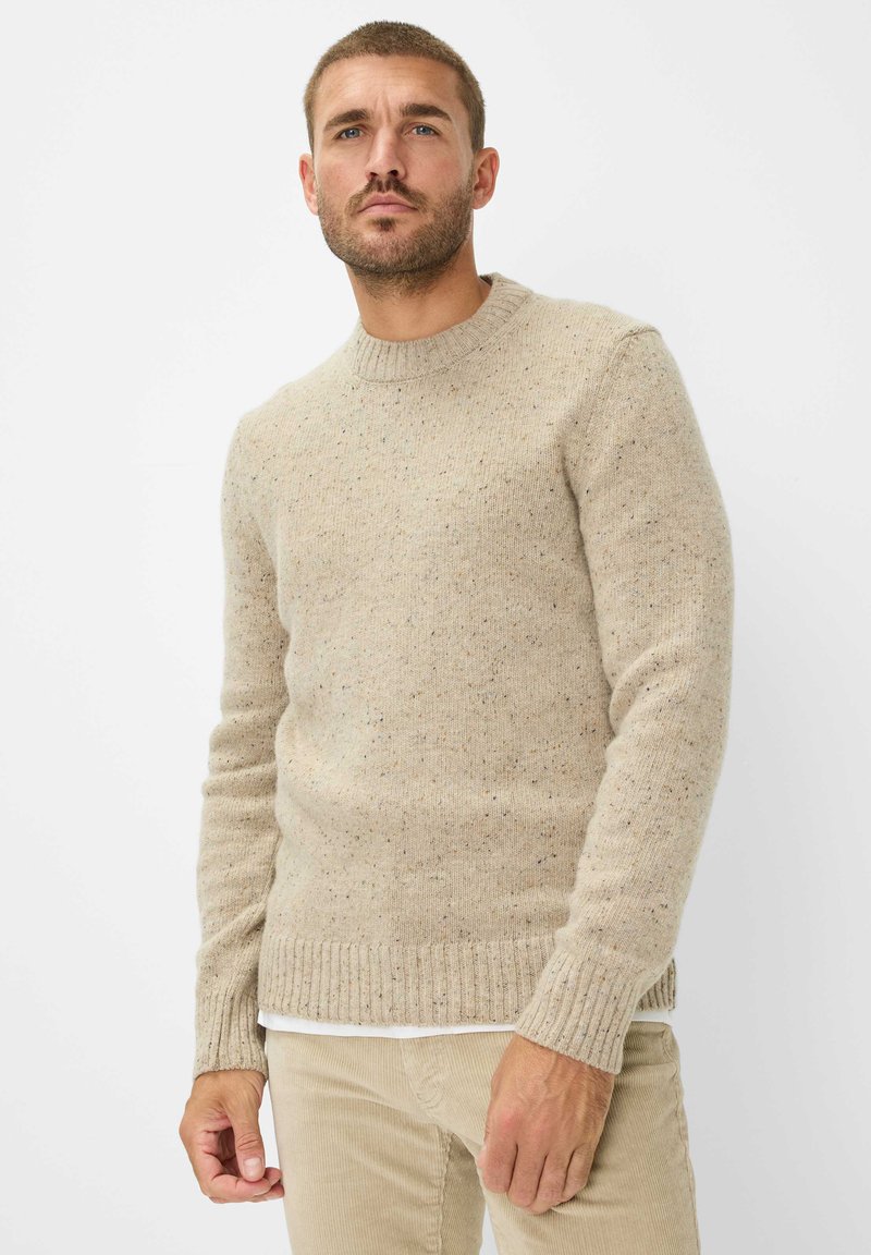Beige Strickpullover mit rundem Ausschnitt, gerippten Bündchen und Saum, einem gefleckten Design und einer taillierten Passform. Betont durch ein schlichtes weißes Hemd darunter.