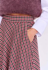 Sukňa zo zmiešaných vlákien v červenej, čiernej a krémovej kockovanej vzore. Má rozšírený strih a bočné vrecká. Mäkká textúra na páse.