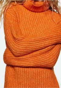 Pomarańczowy sweter z golfem, wykonany na drutach, o prążkowanej strukturze i długich rękawach, z klapowanym kołnierzem i luźnym krojem.