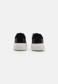 Sneaker in camoscio nero e tessuto a fantasia con suola in gomma bianca. Presenta il marchio sul tallone. La vista posteriore mostra una silhouette curvata.