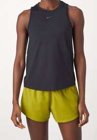 Top deportivo negro sin mangas con escote redondo y ajuste ceñido, combinado con pantalones cortos verdes brillantes con cintura elástica y logo.