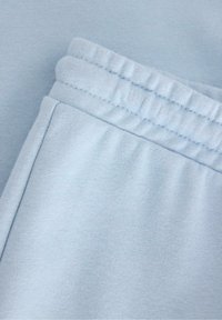 Hellblaues Sportmaterial mit weicher Textur, ausgestattet mit einem elastischen Bund und lockerer Passform. Nahtdetails sind an den Kanten sichtbar.