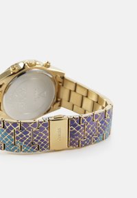 Montre dorée avec un bracelet texturé violet et bleu présentant un motif en écailles. Comprend un fermoir et un fond en acier inoxydable.