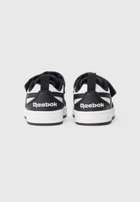 Melnas un baltas Reebok kedas ar mīkstu apkakli, Velcro siksnu, gumijas zoli un sarežģītu izšūšanu sānos.
