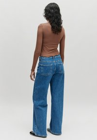 Bruine, lange mouwen, aansluitende top, gecombineerd met losse blauwe denim jeans met een hoge taille en twee achterzakken, gepresenteerd vanuit een achteraanzicht.