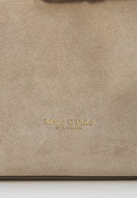 Beżowa torebka z zamszu z teksturowaną powierzchnią i wytłoczonym złotym logo "Marc O'Polo". Prosty design bez dodatkowych elementów czy akcentów.