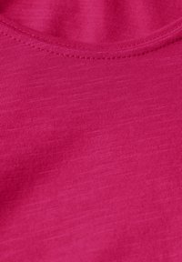 Top aderente rosa realizzato in un morbido tessuto testurizzato con un design a coste e un colletto rotondo, che mostra una finitura liscia e uniforme.