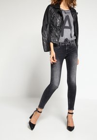 Svart läderjacka över en grå grafisk t-shirt med ett "A", kombinerat med mörka skinny jeans och svarta spetsiga klackar.