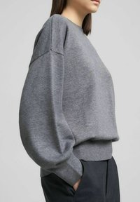 Maglione grigio in maglia con scollo rotondo, spalle scese e polsini a coste. Tessuto morbido e vestibilità comoda, abbinato a pantaloni scuri.