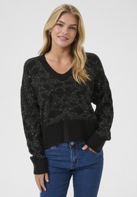 Mustat neulotut neuleet, joissa on V-pääntie, kuvioitu design ja hope glitteriä. Rentoa muotoilua joustinvärkkäillä hihoilla, yhdistetty sinisiin farkkuihin.