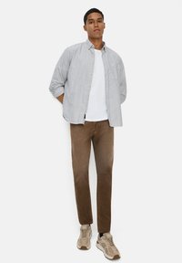 Casual outfit met een blauw-witte gestreepte overhemd, een witte T-shirt, bruine broek en beige sneakers met een gestructureerd ontwerp.