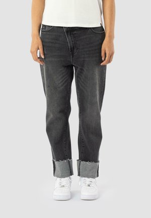 Black ripped jeans featuring frayed hems, a loose fit, and contrasting gray cuffs, paired with white sneakers.
