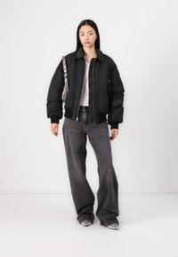 Veste bomber rembourrée noire avec des poignets côtelés, associée à un jean large gris taille haute et des chaussures métalliques à bout pointu. Sac à main en argent en accent.