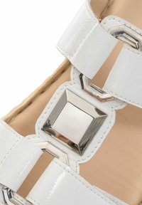 White sandal featuring glossy synthetic straps, silver metallic accents, a square buckle, and a textured footbed with woven detailing.