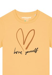 Geel katoenen t-shirt met een bruine hartillustratie en de tekst "houd van jezelf" in een zwarte cursieve lettertype. Korte mouwen, ronde hals.