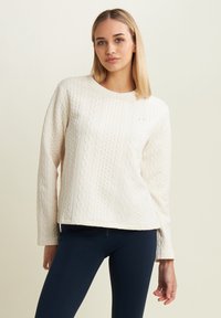 Maglione di colore crema con texture e design a trecce, maniche lunghe e scollatura tonda, abbinato a leggins blu navy.