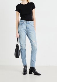 Svart åtsittande t-shirt, ljusblå slitna jeans med hål, svarta klackboots till anklarna och en svart handväska. Enkelt och avslappnat utseende.