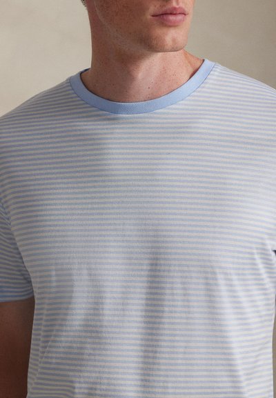 Ανοιχτό μπλε ριγέ μπλουζάκι με μονόχρωμη μπλε λαιμόκοψη. Μαλακό, λείο ύφασμα με οριζόντιες ρίγες και κοντά μανίκια.