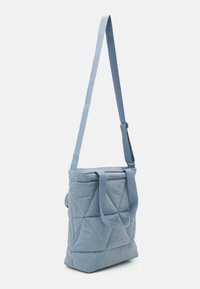 Blå kviltad toteväska med en strukturerad form, tygmaterial, två handtag och en lång justerbar axelrem.