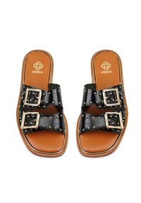 Des sandales à glissière en cuir noir présentent des accents en clous dorés et des détails de boucle. La semelle est beige avec une forme de orteil carrée et une semelle intérieure rembourrée.