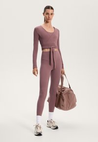 Light mauve athletic set featuring a long-sleeve wrap top with tie and high-waisted leggings. Notable details include texture and fabric finish.