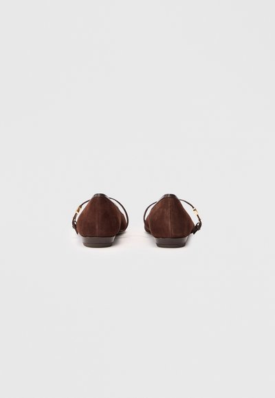 Chaussures plates en daim marron avec une pointe arrondie, des sangles arrière et des accents en métal doré. Le design présente une texture lisse et un style minimaliste.