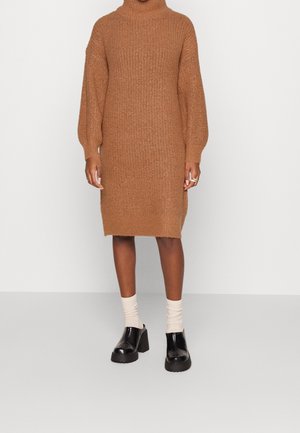 Abito knit marrone con collo alto, maniche lunghe, spacchi laterali e un motivo testurizzato. Abbinato a scarpe con tacco largo nere e calze beige.