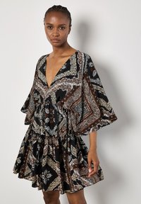 Robe noire longueur genou avec un décolleté en V profond, ornée d'un motif floral et paisley en blanc et marron. Manches courtes et larges, avec une taille froncée.