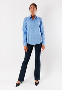 Camicia azzurra a righe con bottoni e maniche lunghe, abbinata a pantaloni a zampa di elefante blu navy e tacchi a punta neri. Tessuto morbido.