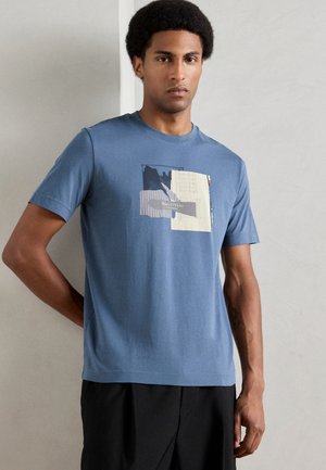 T-shirt en coton bleu avec un col rond, orné d'un imprimé graphique de carrés superposés en marine, beige et à rayures. Manches courtes.