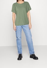 Grøn kortærmet top med rund halsudskæring og struktureret stof, parret med lys blå lige ben jeans og sorte chunky-sole støvler.