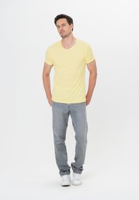 Żółta koszulka z krótkim rękawem i okrągłym dekoltem, zestawiona z jasnoszarymi dżinsami i białymi trampkami; swobodny fason, miękka tekstura.