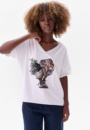Witte T-shirt met korte mouwen met een grote, gedetailleerde graphic van een vrouwenprofiel, versierd met ingewikkelde patronen van een hoofddoek in aardetinten.