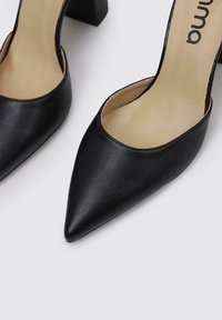 Zapatos de tacón de piel negra con punta afilada y talón abierto, además de un tacón cuadrado. El interior cuenta con una plantilla beige clara, que muestra el nombre de la marca.