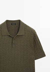 Polo shirt in maglia di colore verde oliva scuro con motivo a trecce, maniche corte e colletto classico. Presenta due bottoni all'apertura del collo.